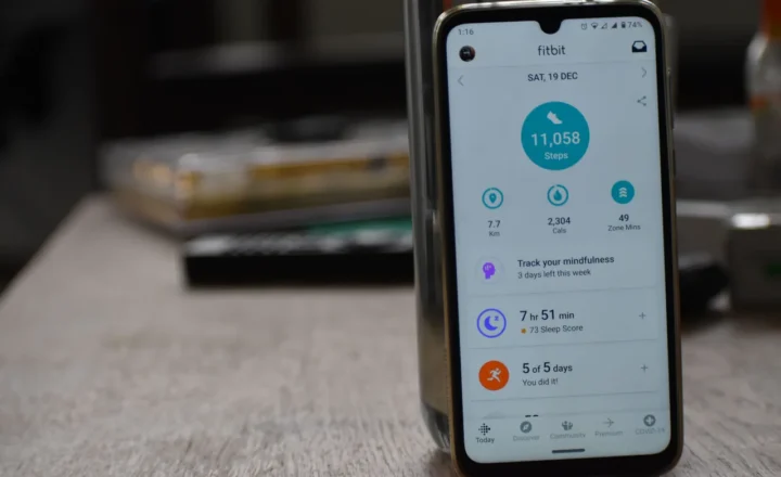 A smartphone standing on a table and displaying a Fitbit activity dashboard.