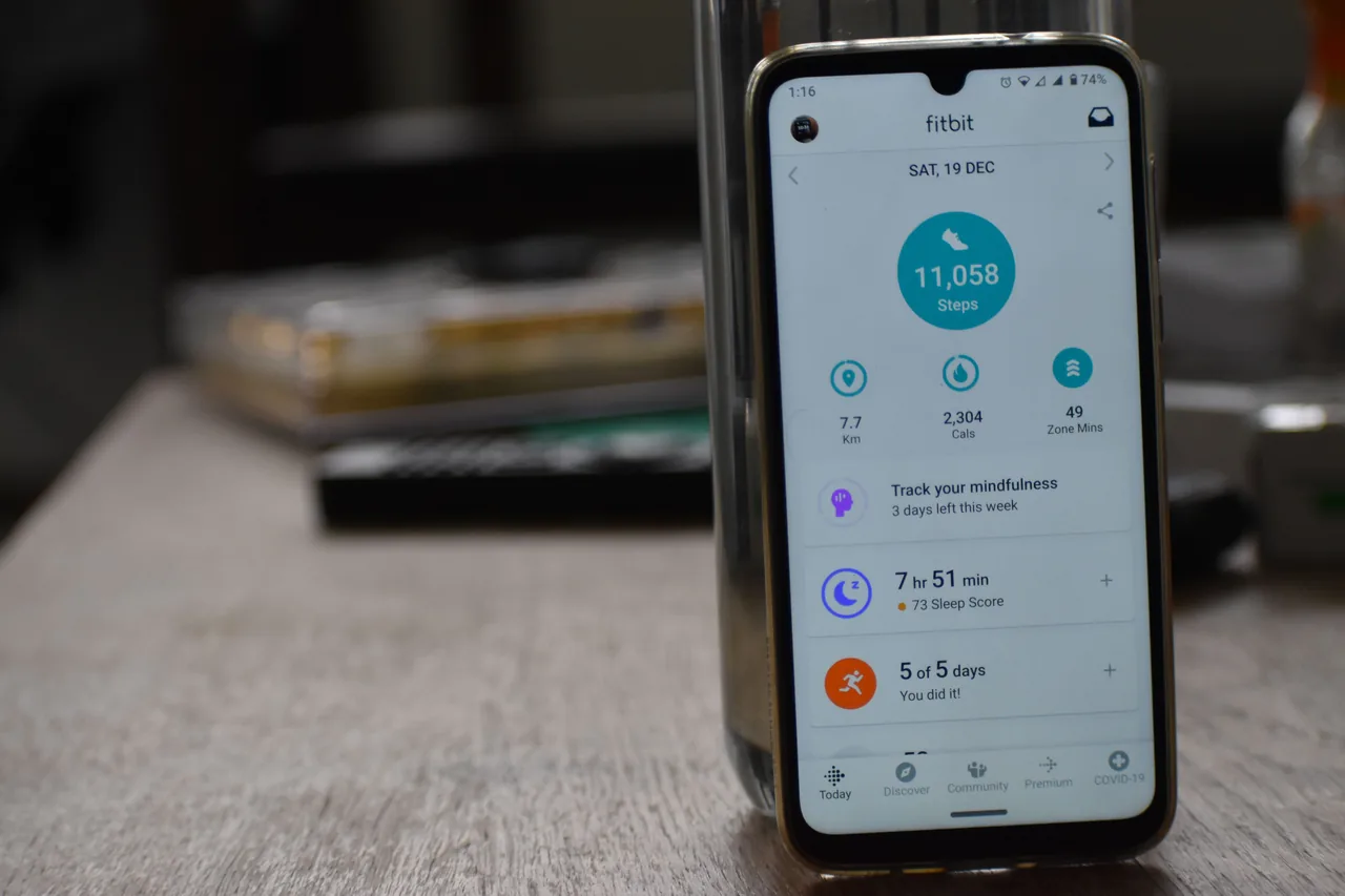 A smartphone standing on a table and displaying a Fitbit activity dashboard.