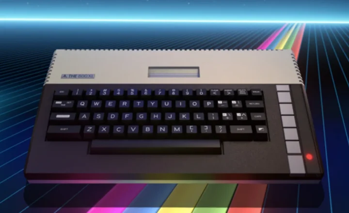 THE800XL computer with a cream upper casing, dark keyboard, vertical row of pale function buttons and glowing red indicator, shown against a blue neon grid with multicolored stripes.