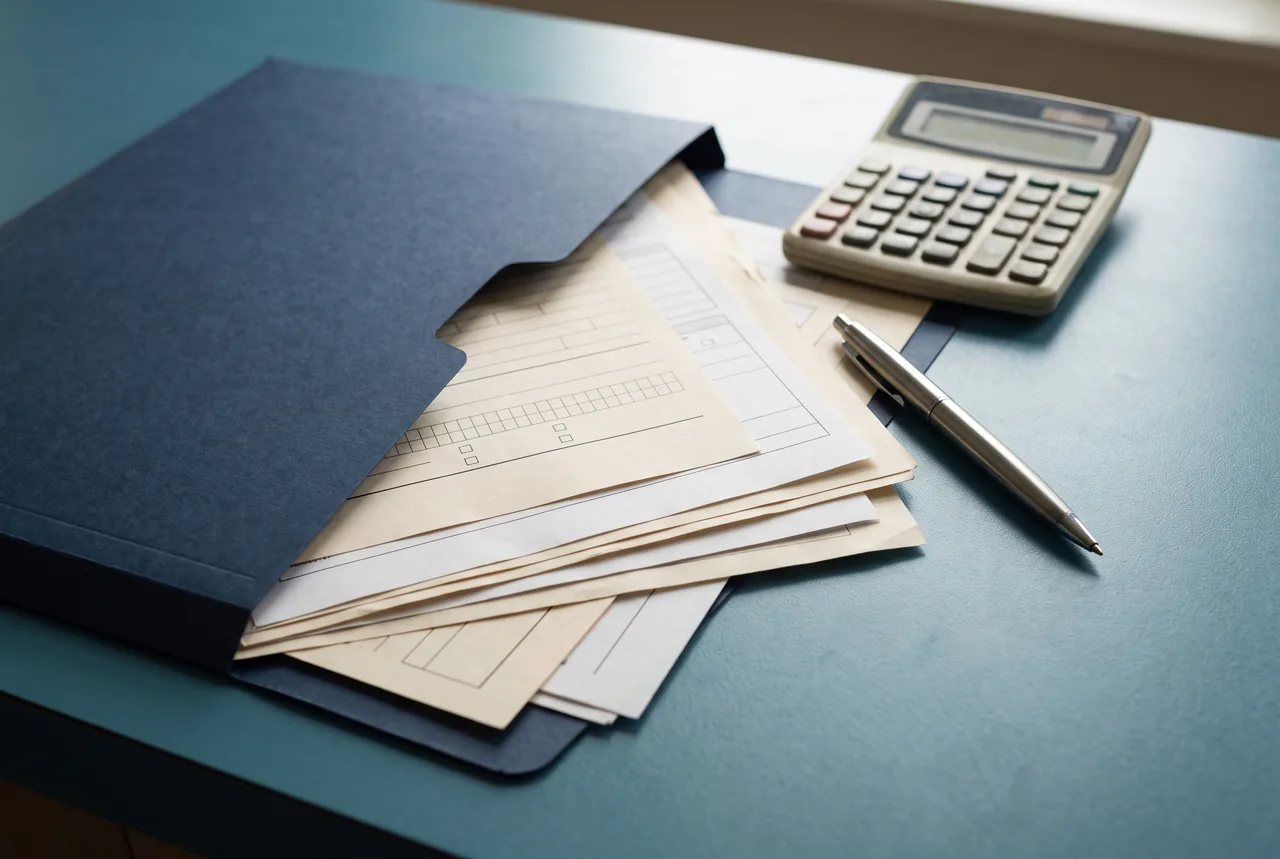 A navy folder holds blank cream forms beside a calculator and a silver pen on a blue surface, shown in a close-up AI-generated illustration.