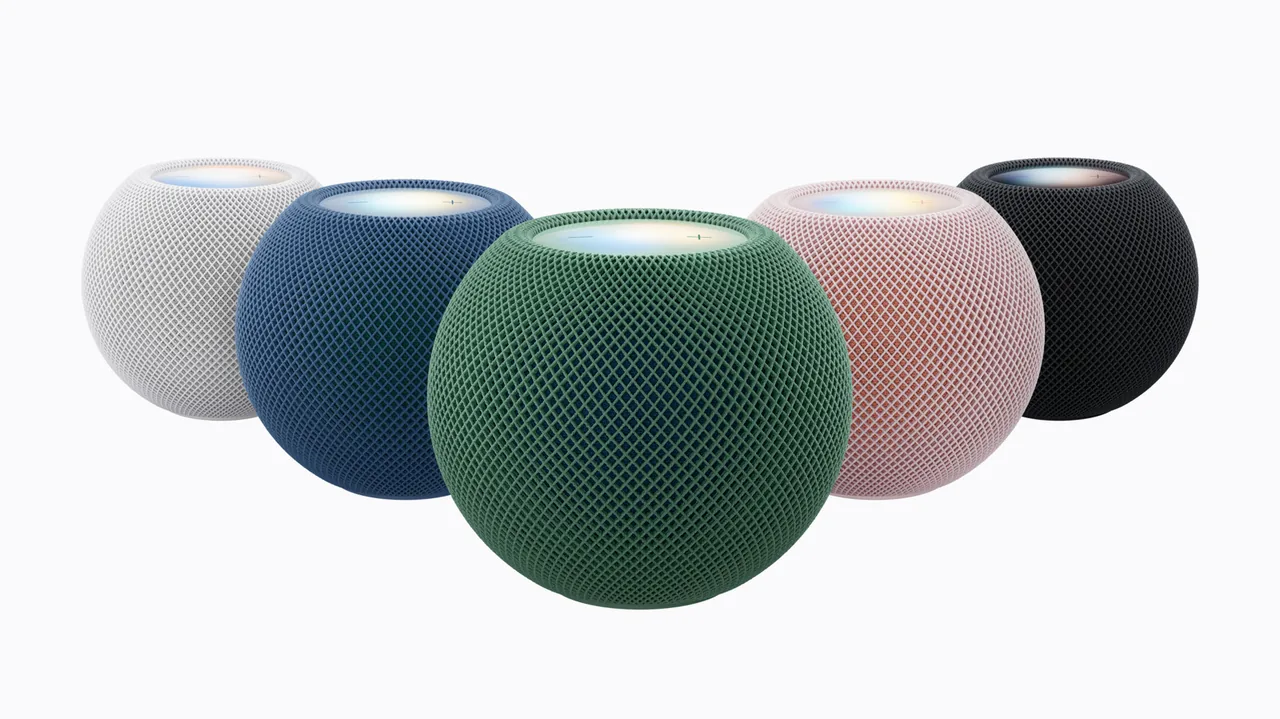 Five spherical mesh-covered smart speakers in white, blue, green, pink, and black on a white background, with illuminated circular touch panels on top. The green speaker sits prominently in front.