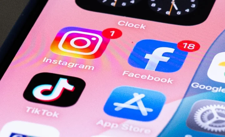 Close-up of a smartphone home screen showing Instagram, Facebook, TikTok and App Store icons on a pink background, with notification badges on Instagram and Facebook.