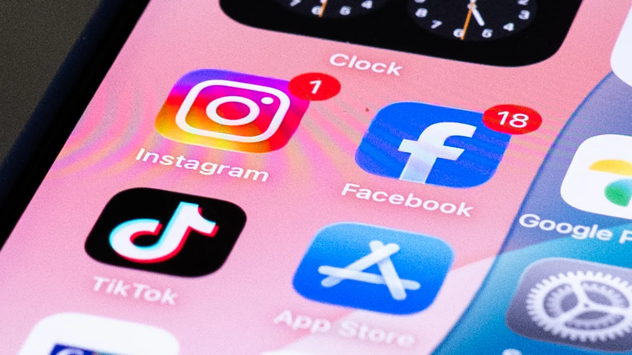 Close-up of a smartphone home screen showing Instagram, Facebook, TikTok and App Store icons on a pink background, with notification badges on Instagram and Facebook.