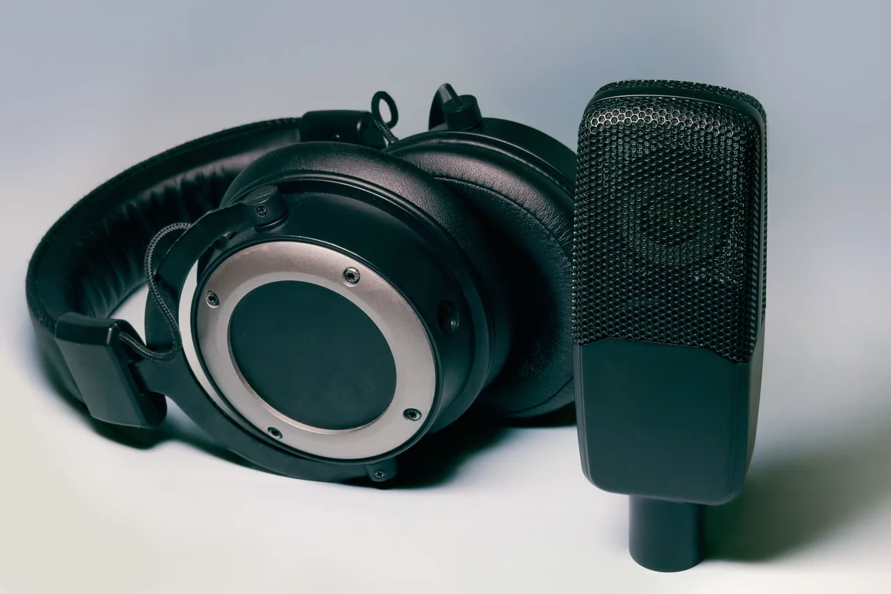 Black over-ear headphones beside a black microphone on a light-colored surface.