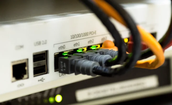 Black and orange Ethernet cables plugged into a white network device, with green indicator lights.